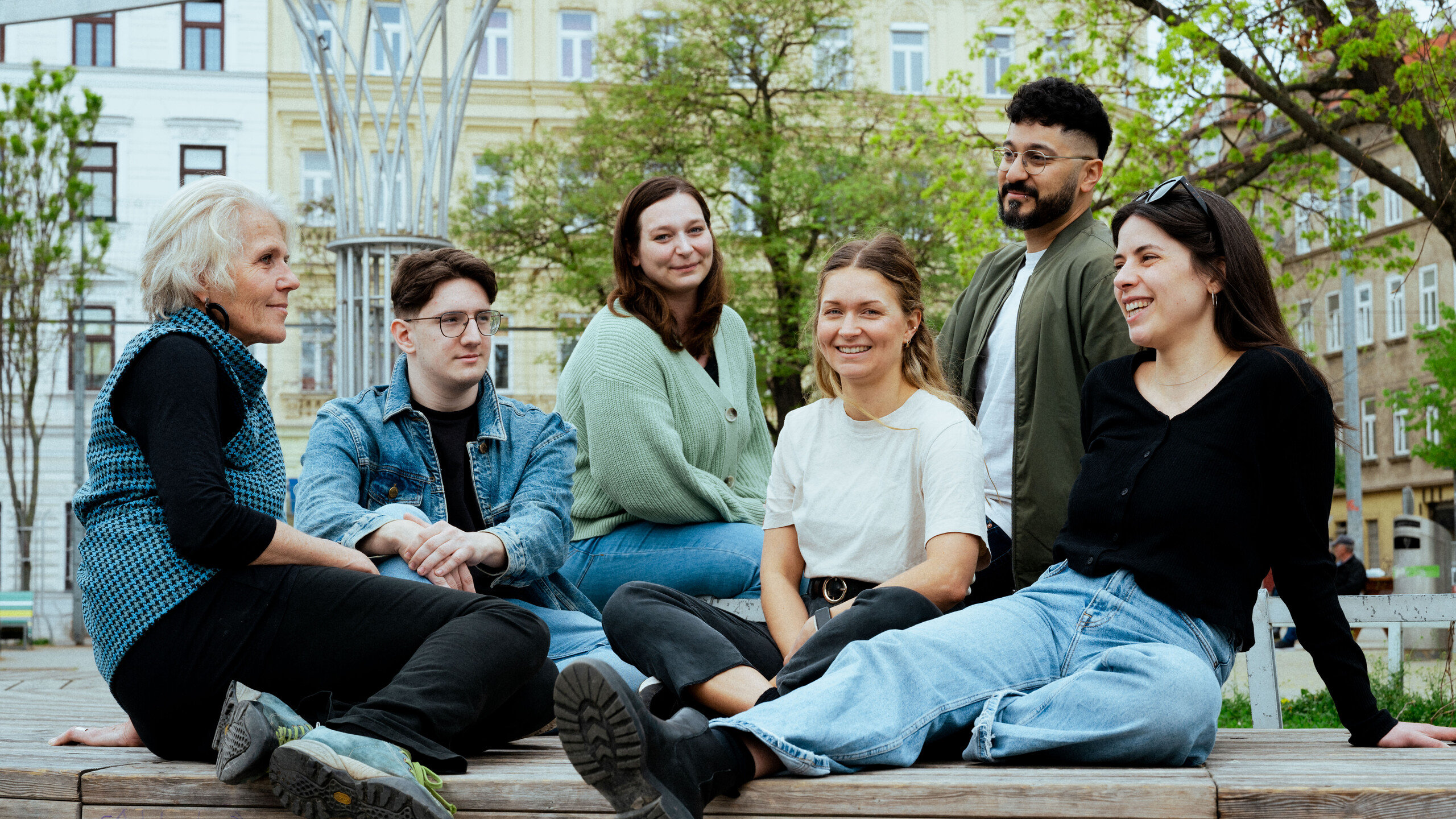 Menschengruppe im Gespräch  Sechs Menschen sitzen in einer Gruppe im Park zusammen und unterhalten sich